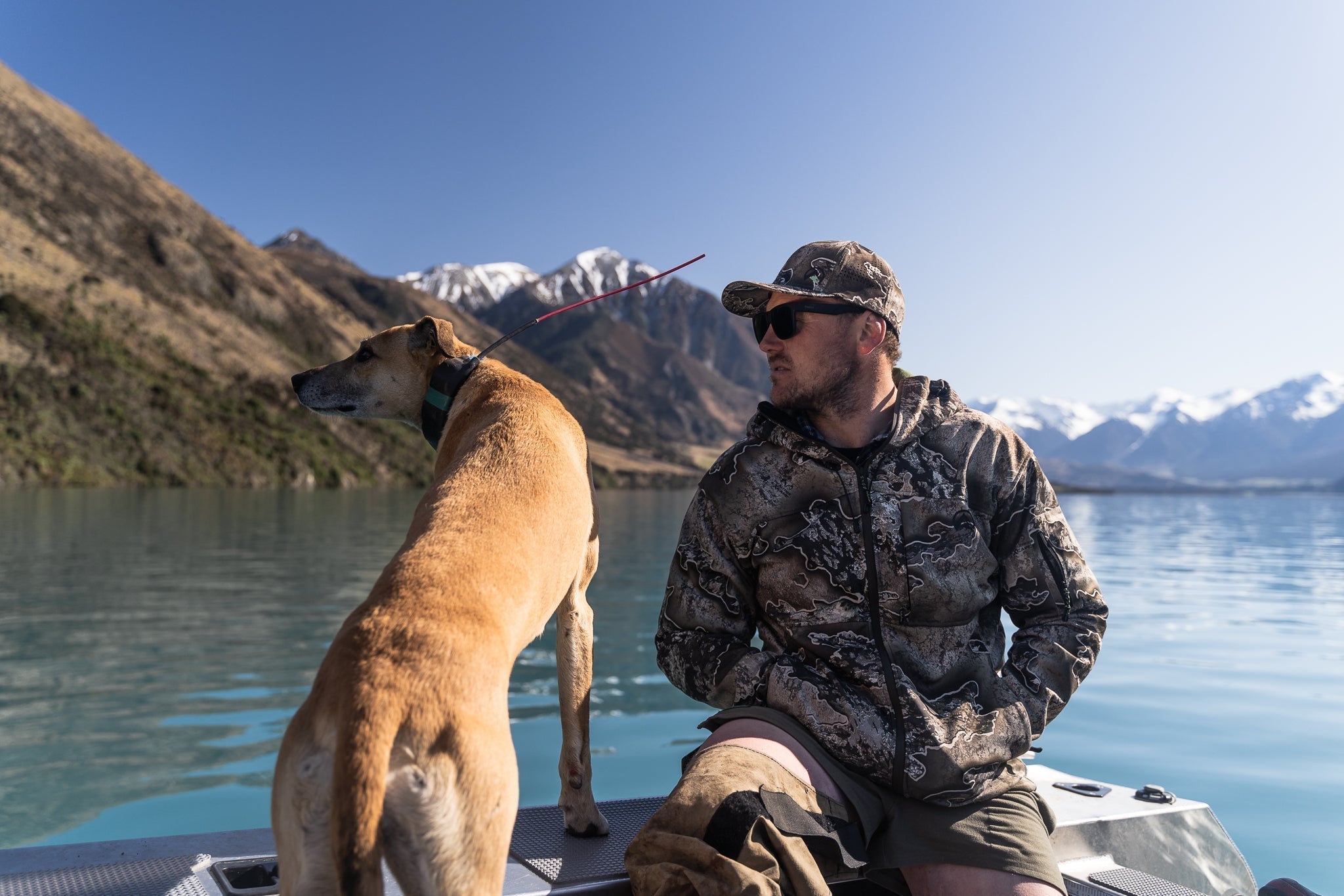 Hunter and dog on a boat in New Zealand, preparing for an outdoor adventure surrounded by alpine mountains.